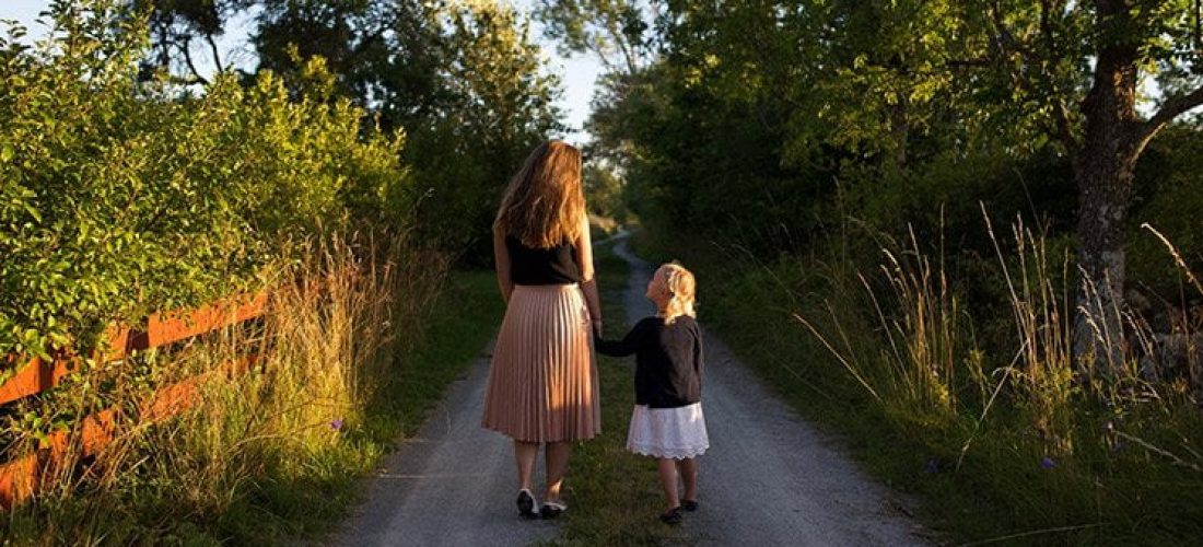 Une mère accompagne son enfant sur un chemin de campagne.